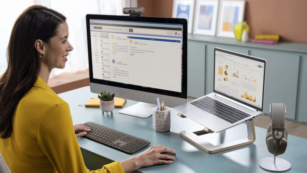 An image of a woman sitting and facing a laptop and a monitor