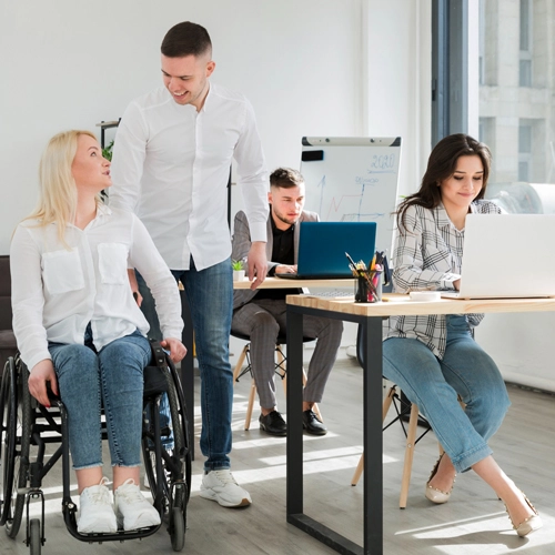 A woman in a wheelchair engages with a colleague, while others focus on laptops.