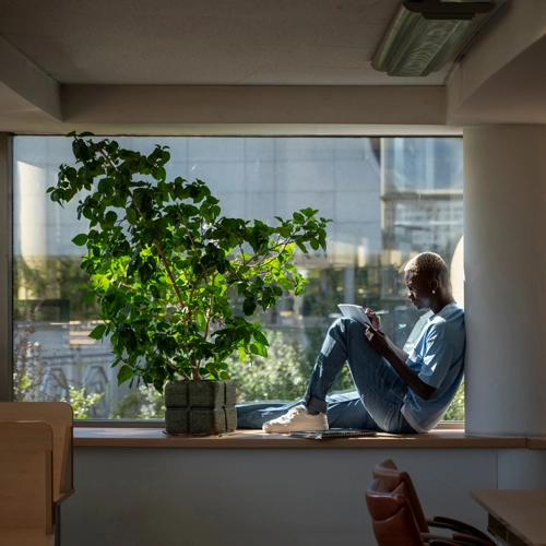 An image of a man sitting on a ledge with his back against a column while reading from a piece of paper.
