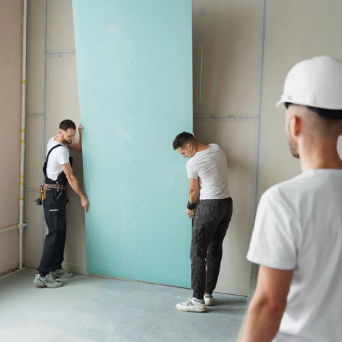 An image showing three men installing a panel board with a drill.