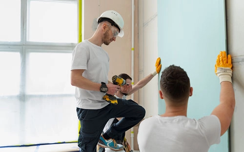 An image showing three men installing a panel board with a drill.