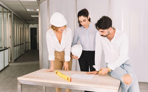 An image of three white hat workers looking at a document laid flat on the table.