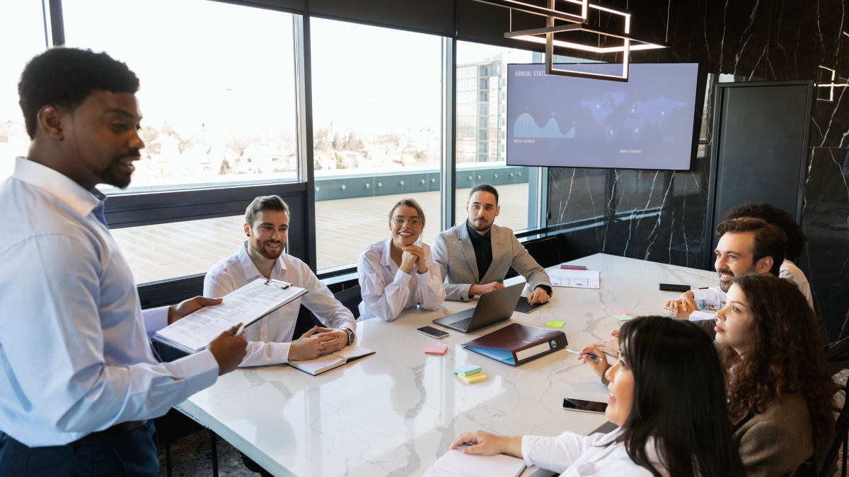 Business team in a meeting, a man presenting to colleagues seated around a large conference table.
